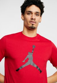Rød bomulds t-shirt med rund halsudskæring, der har et stort sort Jordan-logo grafik på forsiden, glat tekstur og korte ærmer.