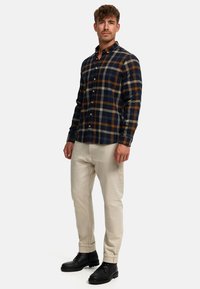 Flanellskjorte i marineblå, beige og brun rutete, med knappespisskrage; kombinert med beige bukser og svarte snørestøvler.