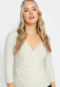 Helle beige, langärmlige Bluse mit V-Ausschnitt und Wickeldesign. Strukturierter Stoff mit feinen Rippdetails; tailliert.