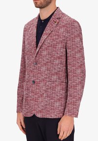Blazer a motivo a spina di pesce rosso e bianco con rever a punta, due bottoni e una tasca. Indossato sopra una polo scura.