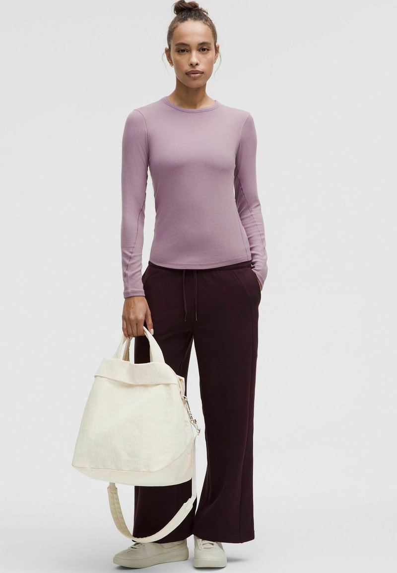 Blusa a maniche lunghe di lavanda abbinata a pantaloni larghi di un rosso borgogna scuro e una borsa crema, con un design pieghevole e una tracolla regolabile.