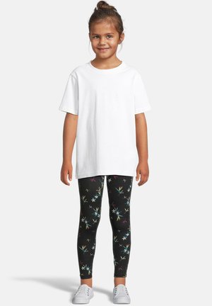 Hvit bomullst-skjorte sammen med svarte leggings med et fargerikt blomstermønster. Hvite sneakers fullfører antrekket.