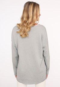 Maglietta a maniche lunghe grigia chiara con orlo arrotondato, vestibilità comoda e texture morbida, con spalle scese e dettagli minimi.