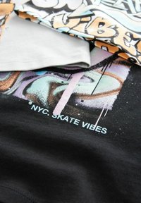 Schwarzes Baumwoll-T-Shirt mit einem bunten Graffiti-Druck in Pink, Grün und Blau, auf dem der Text "NYC. SKATE VIBES" auffällig präsentiert wird.