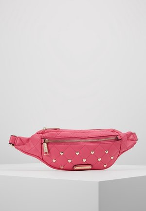 Sac banane matelassé rose avec des clous dorés en forme de cœur, poche zippée avant et sangle ajustable sur un présentoir blanc.