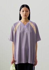 Maglietta in jersey viola a vestibilità ampia con scollo a V e dettagli in rete beige chiaro. Presenta un piccolo logo sul davanti e una silhouette rilassata.