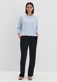 Hellblauer, gerippter Pullover mit Bootsausschnitt und langen Ärmeln, kombiniert mit schwarzen, hoch taillierten Hosen mit vorderen Nähten.