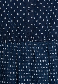 Marindress med vita prickar, knapprad, plisserad kjolstruktur och mjukt tygmaterial.