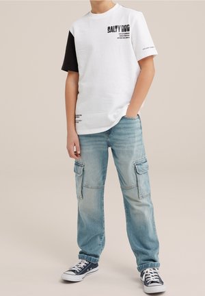 Niño con camiseta de manga corta blanca y negra con la inscripción "SALTY DOG", vaqueros cargo azul claro y zapatillas azul marino con cordones blancos.