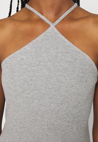 Harmaa ilmanhihaista toppia, joka on valmistettu ribbikankaasta. Vaatteessa on ristikkäinen olkainten muotoilu kaula-aukossa ja se on tiiviisti istuva.