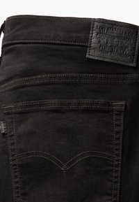 Poche arrière d'un jean en denim noir avec des coutures marron et un patch en cuir noir de la marque Levi Strauss & Co. sur la ceinture.