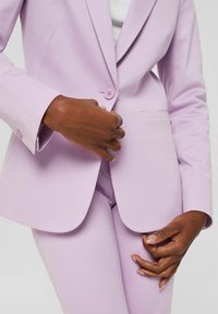 Blazer sur mesure lilas en tissu lisse avec une fermeture à un seul bouton et des revers crantés, associé à un pantalon ajusté assorti.