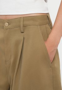 Khaki püksid sirge lõikega, ees voldid ja küljetaskud. Kangas on sileda tekstuuriga ning lukuga. 