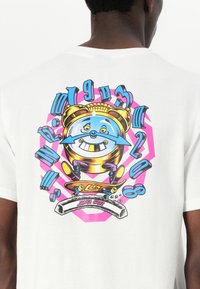 White cotton t-shirt featuring a colorful graphic of a smiling alarm clock on a pink and blue design, with skateboarding elements and "Santa Cruz" text.