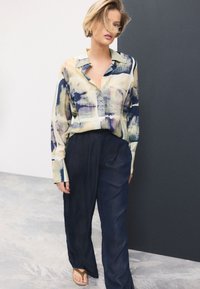 Button-up shirt in pastel colors with an abstract pattern, paired with dark, wide-leg trousers and flip-flops. Soft, lightweight fabric.