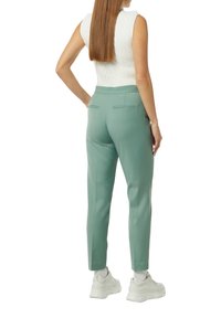 Mintgrüne, maßgeschneiderte Hose mit mittelhoher Passform, ausgestattet mit zwei Gesäßtaschen und einer glatten Textur, kombiniert mit weißen Sneakers.