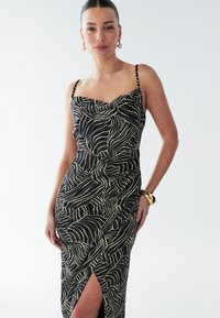 Black dress with cream abstract wave pattern, cowl neckline, slim straps, side slit, and draped design. Smooth fabric with a fitted silhouette.