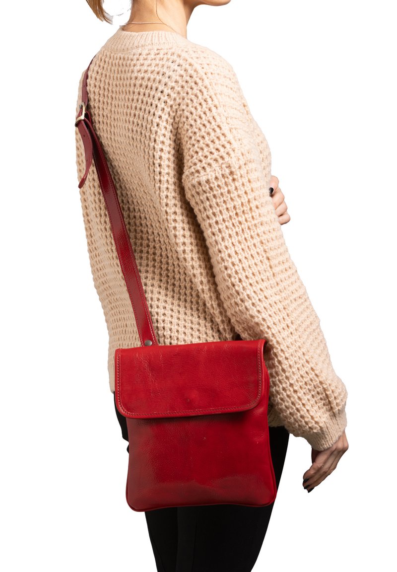 Borsa a tracolla rossa in pelle con chiusura a patta, tracolla regolabile, texture liscia e forma quadrata, indossata con un maglione lavorato a maglia beige chiaro.