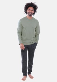 Langärmliges olivgrünes Hemd kombiniert mit schwarzen, gemusterten Hosen. Das Hemd ist figurbetont, und die Hose weist ein dezentes geometrisches Muster auf.