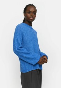 Blauwe gebreide trui met een textuurafwerking, ronde halslijn en lange mouwen. Zacht materiaal met een ontspannen pasvorm, gecombineerd met donkergrijze broek.