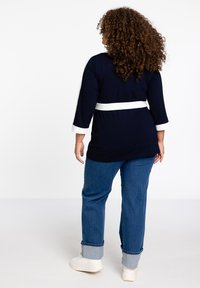 Marineblaues Tunika-Oberteil mit weißen Akzenten und dreiviertelärmligen Ärmeln, kombiniert mit locker sitzenden Jeans im Denim-Stil mit aufgerollten Säumen und weißen Sneakers.