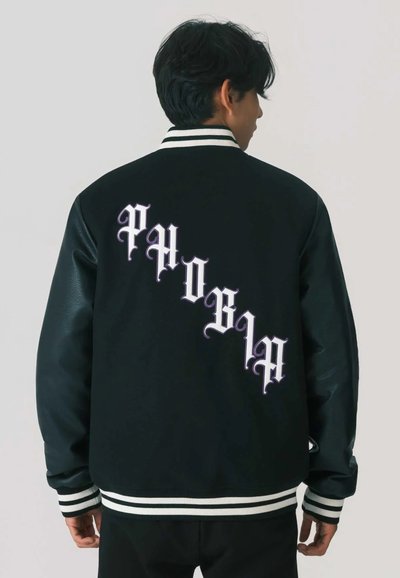 Giacca varsity nera con maniche in pelle, polsini a righe bianche e nere e testo ricamato "PHOBIA" in viola sul retro.