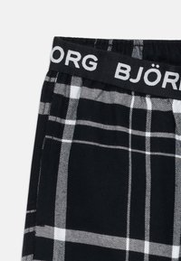 Tecido xadrez em preto e branco com cintura elástica mostrando o texto "BJÖRN BORG" em letras brancas.