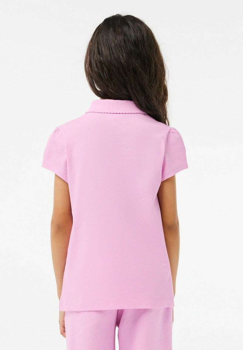 Polo shirt rose à manches courtes avec un col festonné et une finition en tissu texturé, vue de dos, révélant une coupe décontractée.