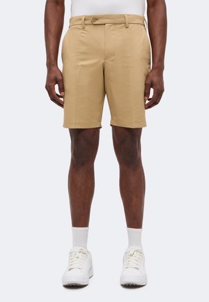 Homme portant un short beige sur mesure, des chaussettes blanches montantes et des baskets blanches, debout les mains détendues le long du corps.
