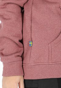 Maroon hoodie in a textured fabric, featuring a side pocket with a small blue and yellow Swedish flag emblem.