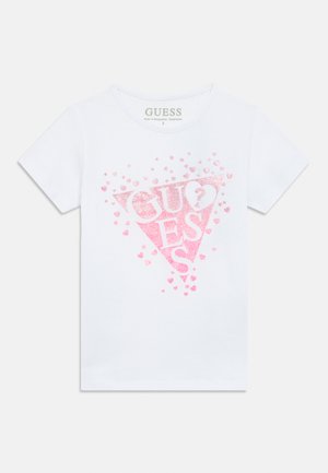 Camiseta blanca de manga corta con un gran triángulo rosa brillante que incluye la palabra "GUESS" y pequeños corazones rosas dispersos.