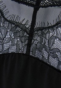 Czarna bielizna, która ma delikatną koronkową górę z kwiatowymi wzorami oraz gładką dolną część. Materiał jest przezroczysty o miękkiej teksturze.