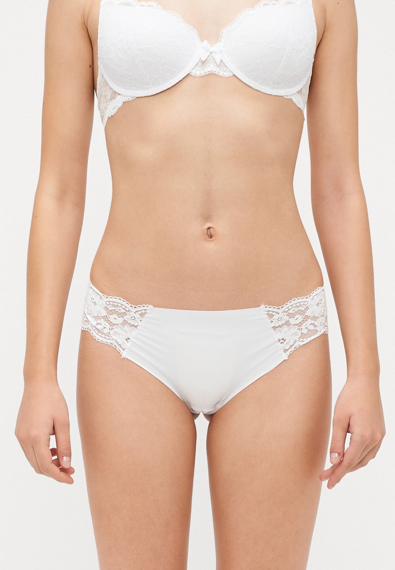 Fehér csipkés és selyem bikini alsó, sima elülső résszel és virágmintás csipke oldalakkal. Egyszerű dizájn, passzoló díszítéssel a széleken.