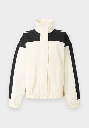 Veste à col montant avec épaules et bras supérieurs noirs, corps et manches crème, poignets élastiques, et pas de fermetures visibles à l'avant.