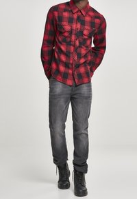 Röd och svart rutig skjorta med knappar och två bröstfickor, i kombination med grå jeans och svarta snörkängor.