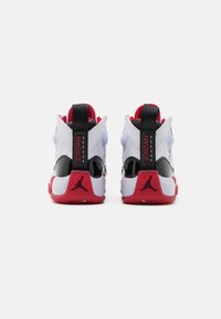 Sneakers med en ovandel i vitt och svart läder, röda detaljer, klack i svart lackläder och en röd sula med Jordan-logotypen.