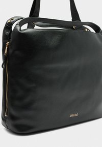 Schwarze Ledertasche mit glatter Textur, ausgestattet mit goldenen Akzenten und einem deutlich auf der Vorderseite platzierten Markenlogo.