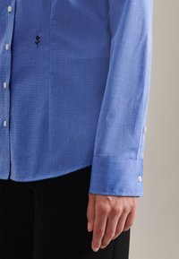 Lichtblauw shirt van textuurstof met een bloemendetail in borduurwerk en witte knopen, met een ingenomen manchet en een gestructureerde kraag.