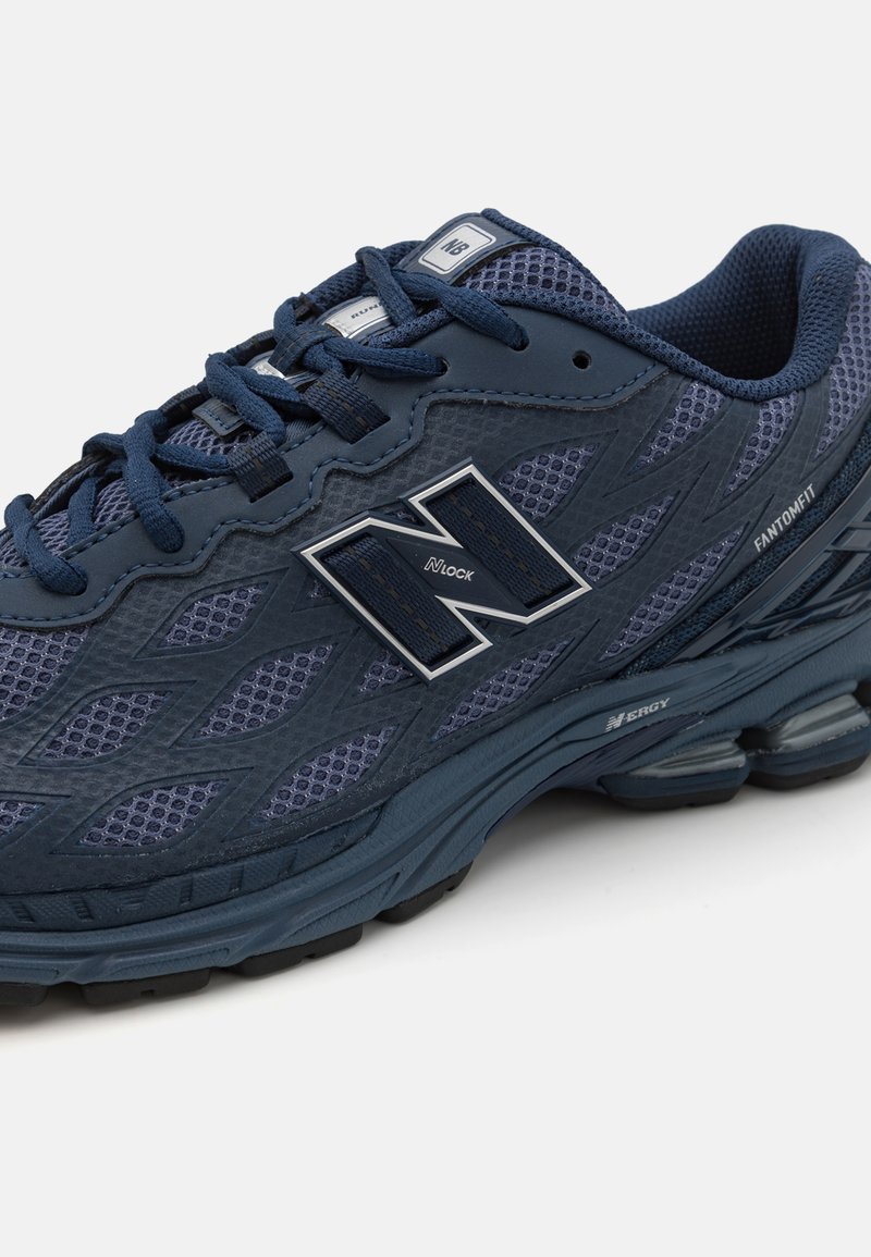Chaussure de course pour homme en bleu marine avec tige en maille, superpositions synthétiques et logo N. Caractéristiques d'une semelle amortie et d'accents texturés.