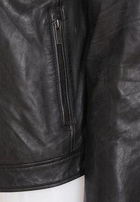 Svart läderjacka med en dragkedjeficka, slät textur och skräddarsydd design med en subtil glans och rundad nederkant.