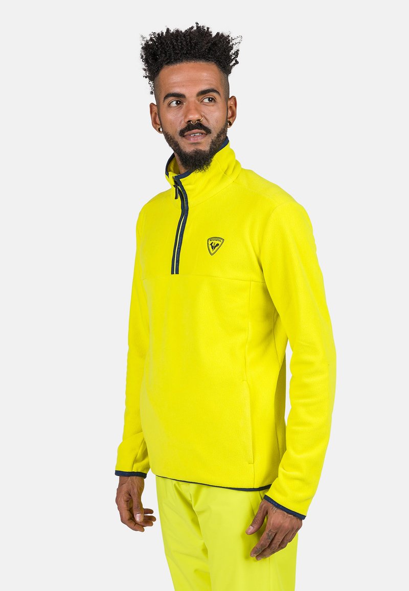 Pullover giallo in pile con mezza zip, colletto alto e accenti blu navy. Presenta un logo sul petto e una texture morbida.