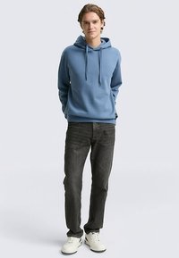 Ljusblå bomullshoodie med dragsnören, med avslappnad passform. Kombinerad med mörkgrå jeans och vita sneakers. Enkel och avslappnad design.