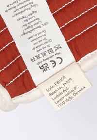 Red cotton fabric with a quilted pattern; off-white label featuring care instructions and product details sewn into the edge.