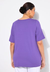 Lila kortärmad topp med rund halsringning, mjuk textur och avslappnad passform, med en lätt sänkt nederkant och inga synliga mönster eller detaljer.