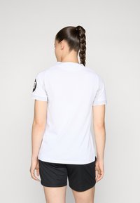 Chemise de sport blanche à manches courtes avec un col rond, assortie à un short noir. Présente un tissu texturé et des accents de manches contrastés.