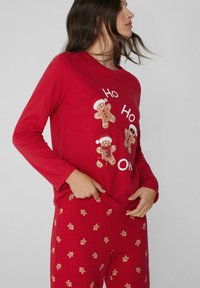 Parte superior de pijama roja de manga larga con gráficos de muñeco de jengibre y texto. Los pantalones rojos a juego presentan un patrón repetitivo de muñecos de jengibre.