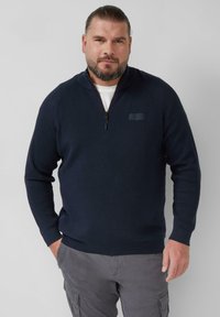 Navyblauwe geribbelde trui met een ritskraag, voorzien van een klein patchdetail op de borst en lange mouwen. Comfortabele pasvorm.