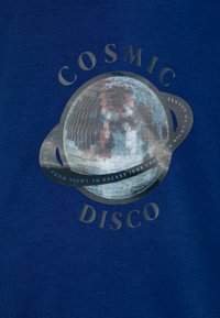 La tela de algodón azul presenta un gráfico de una bola de discoteca rodeada por el texto "COSMIC DISCO" en acentos metálicos plateados y rosas.