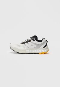 Weißer und schwarzer Sportschuh mit orangefarbenen Akzenten, Schnürdesign, Obermaterial aus Mesh und "SCARPA"-Markierung auf der dicken Sohle.