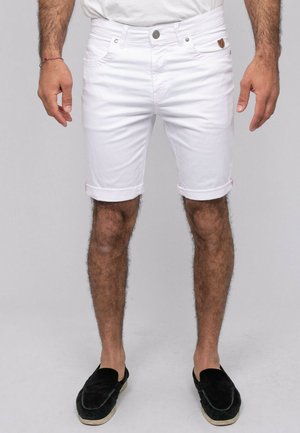 Short blanc pour homme à ourlet roulé avec poches avant et chaussures noires sans lacets, présenté de la taille aux pieds sur fond gris.
